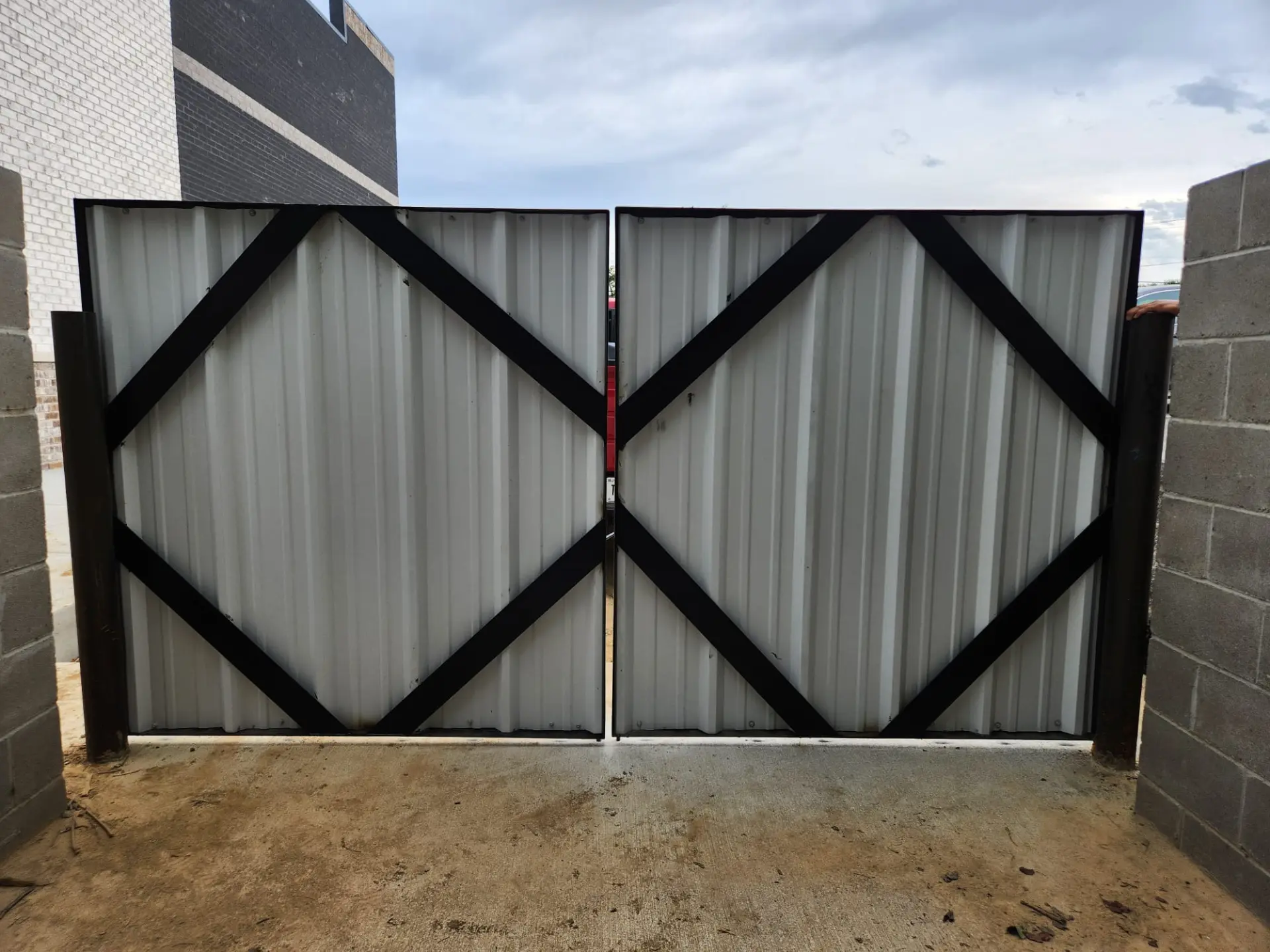 Finished steel-framed double driveway gate with white corrugated panels and black diagonal bracing