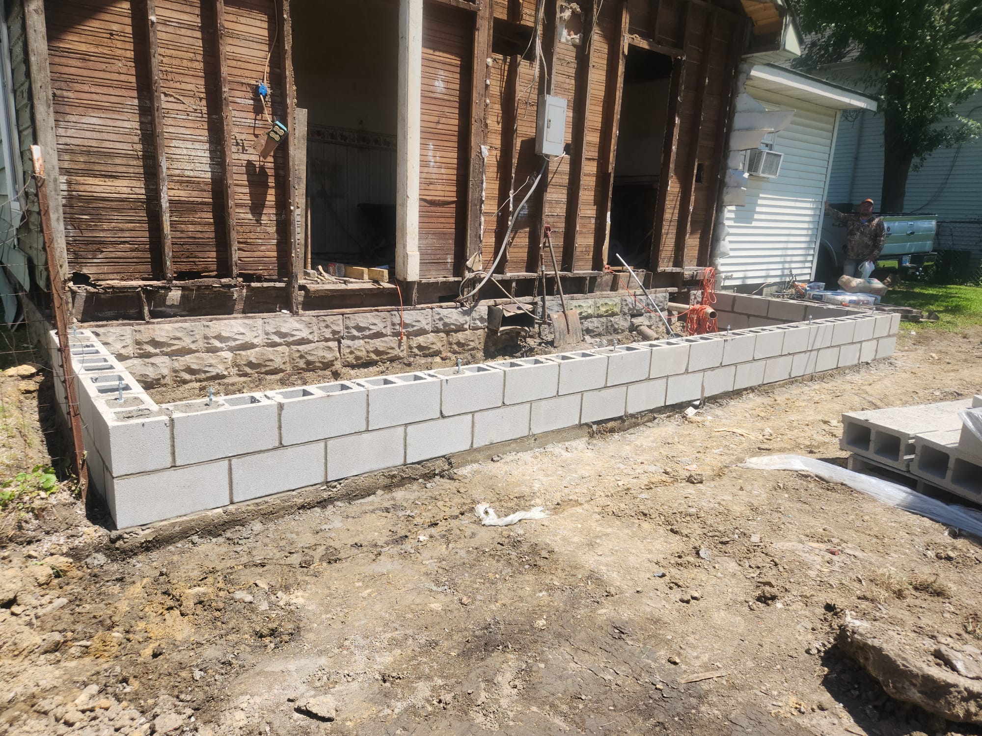 New concrete block foundation wall laid around a stripped timber-framed house with anchor bolts set in the top course
