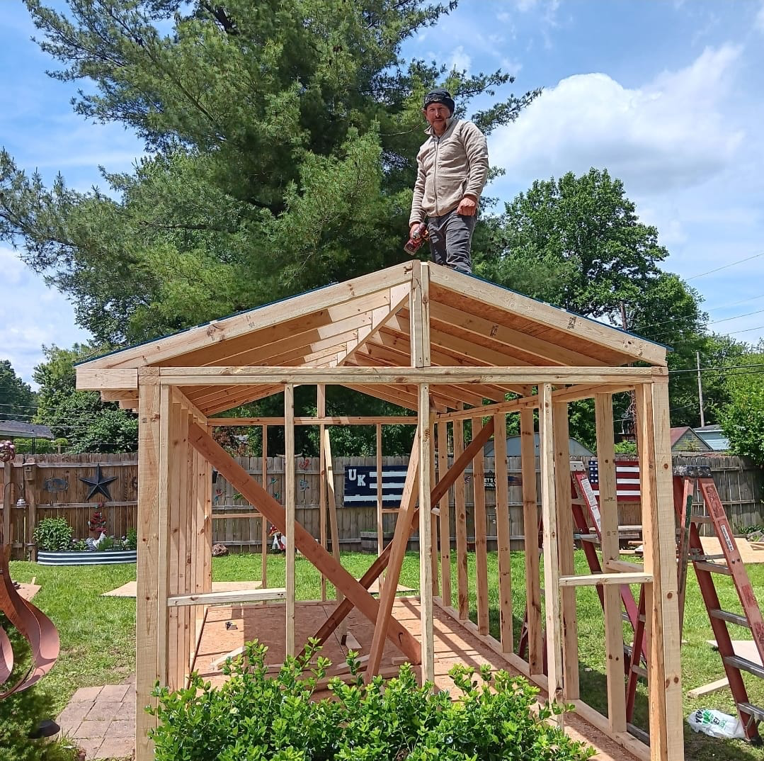 Timber pavilion frame and gable roof structure being built over a backyard patio area