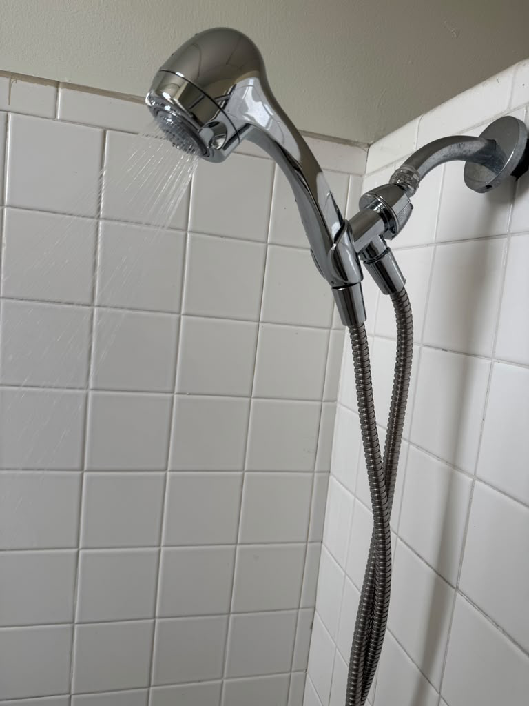 New chrome handheld shower head running water on a white tiled shower wall with flexible hose
