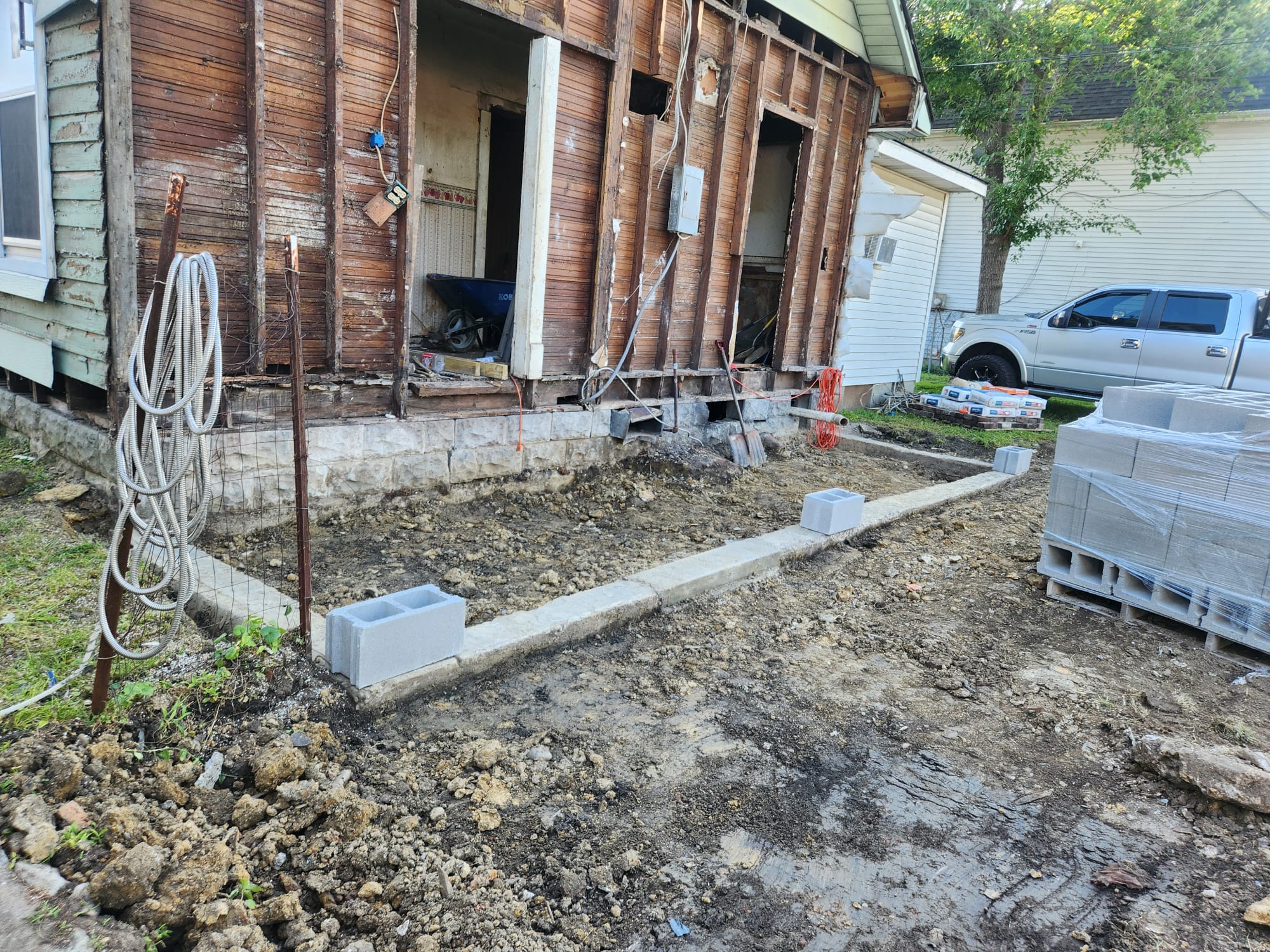 Poured footing and rebar set out for a rear addition beside a stripped-back timber-framed house