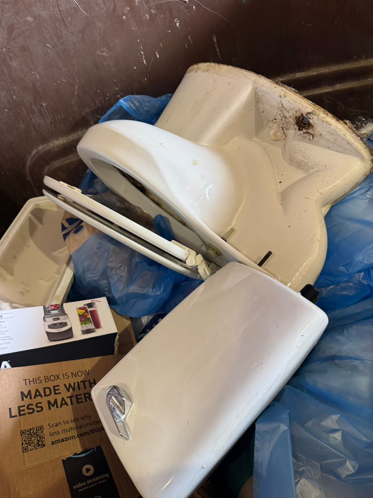 Old toilet bowl, tank and seat removed from site and loaded into a dumpster for disposal