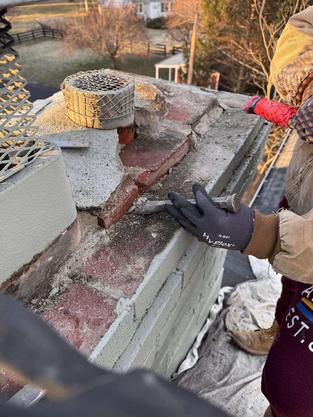 Mason chiselling out failed brick and mortar from the chimney crown during a rebuild