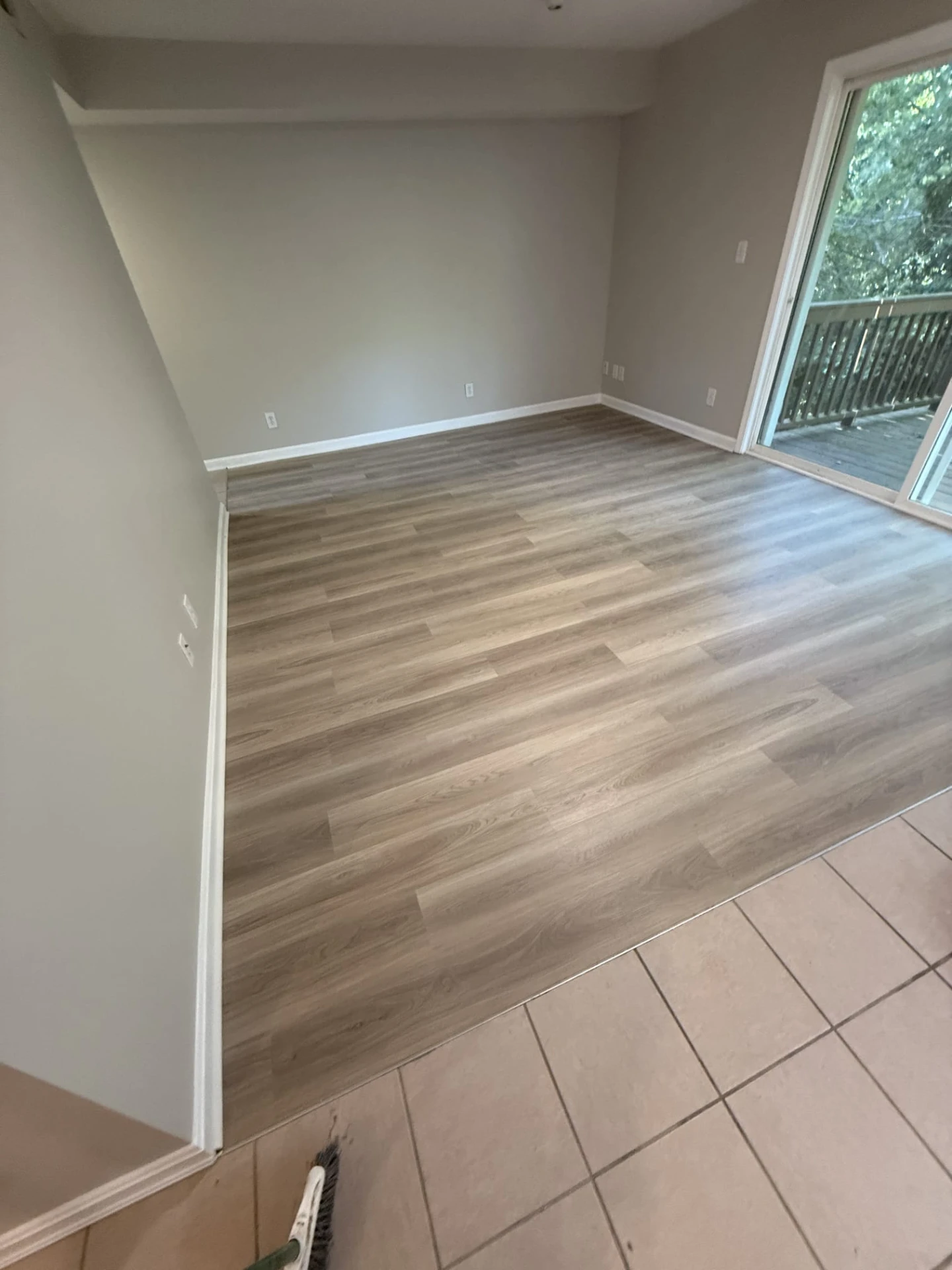 After: finished light oak LVP floor with new white baseboards meeting the existing tile