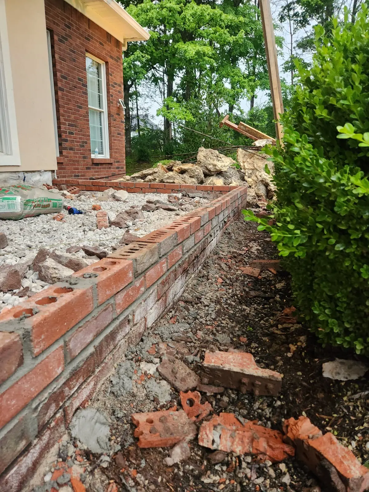 Red brick retaining wall under construction beside a brick home, with mortar beds and stepped courses