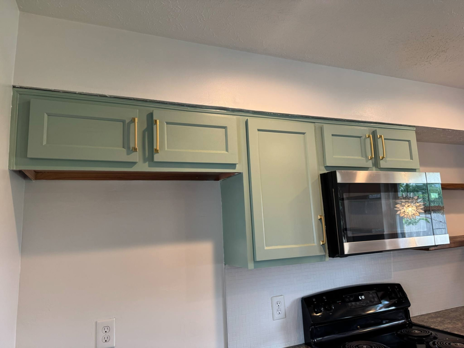 Freshly repainted sage green upper cabinets with new brass handles above the range
