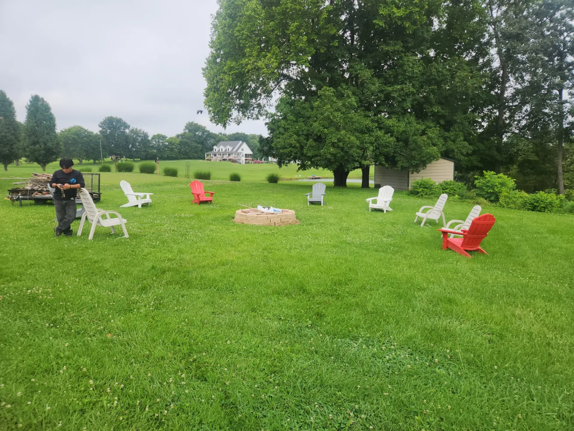 Before: patchy backyard lawn with a bare block fire pit and scattered chairs ahead of repair