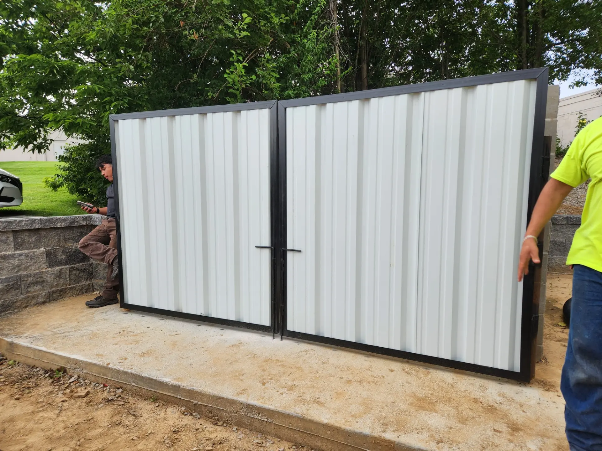 Crew setting a custom steel-framed metal driveway gate between block piers