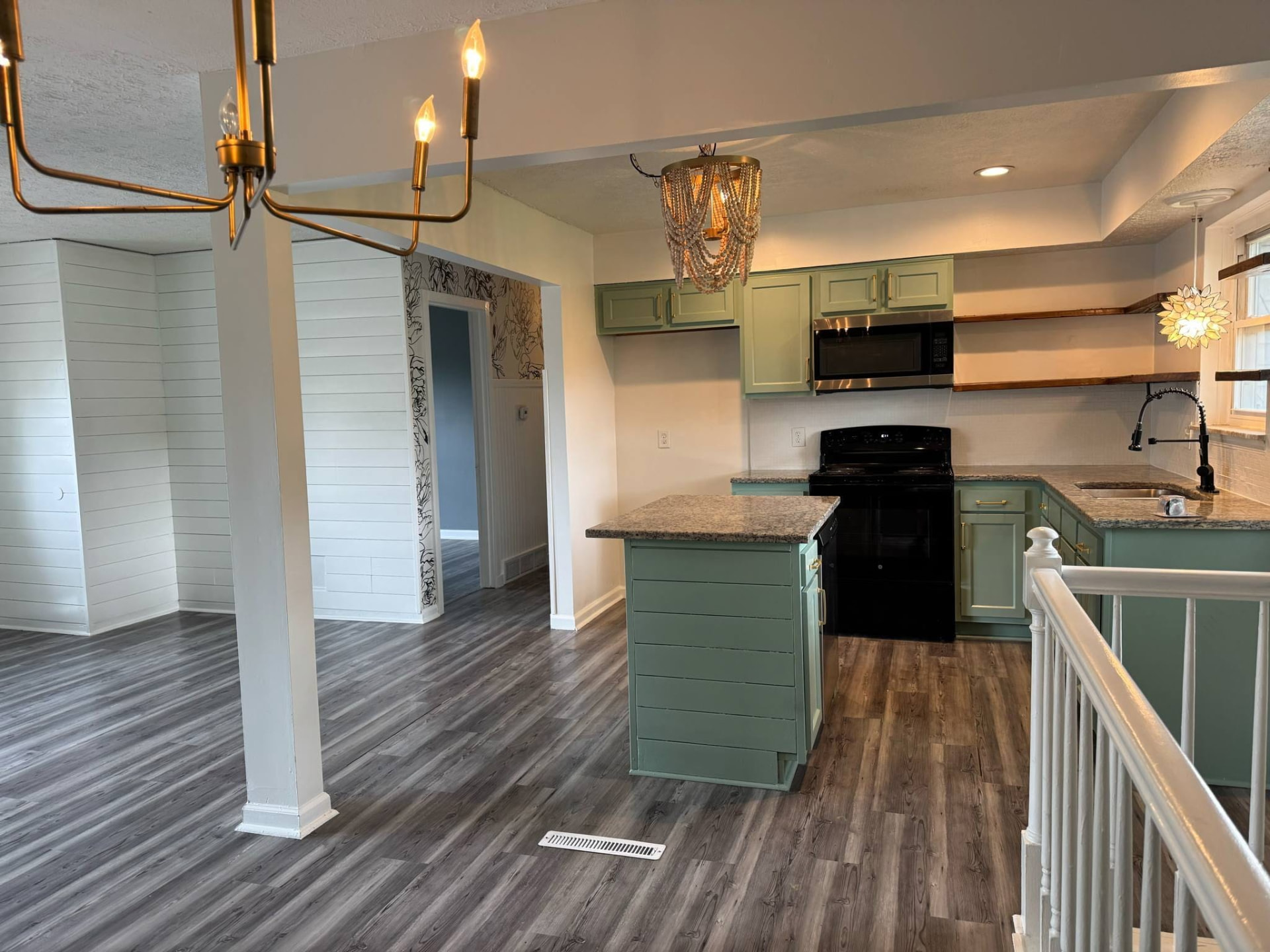 Renovated open-plan kitchen with sage green cabinets, granite island and grey plank flooring