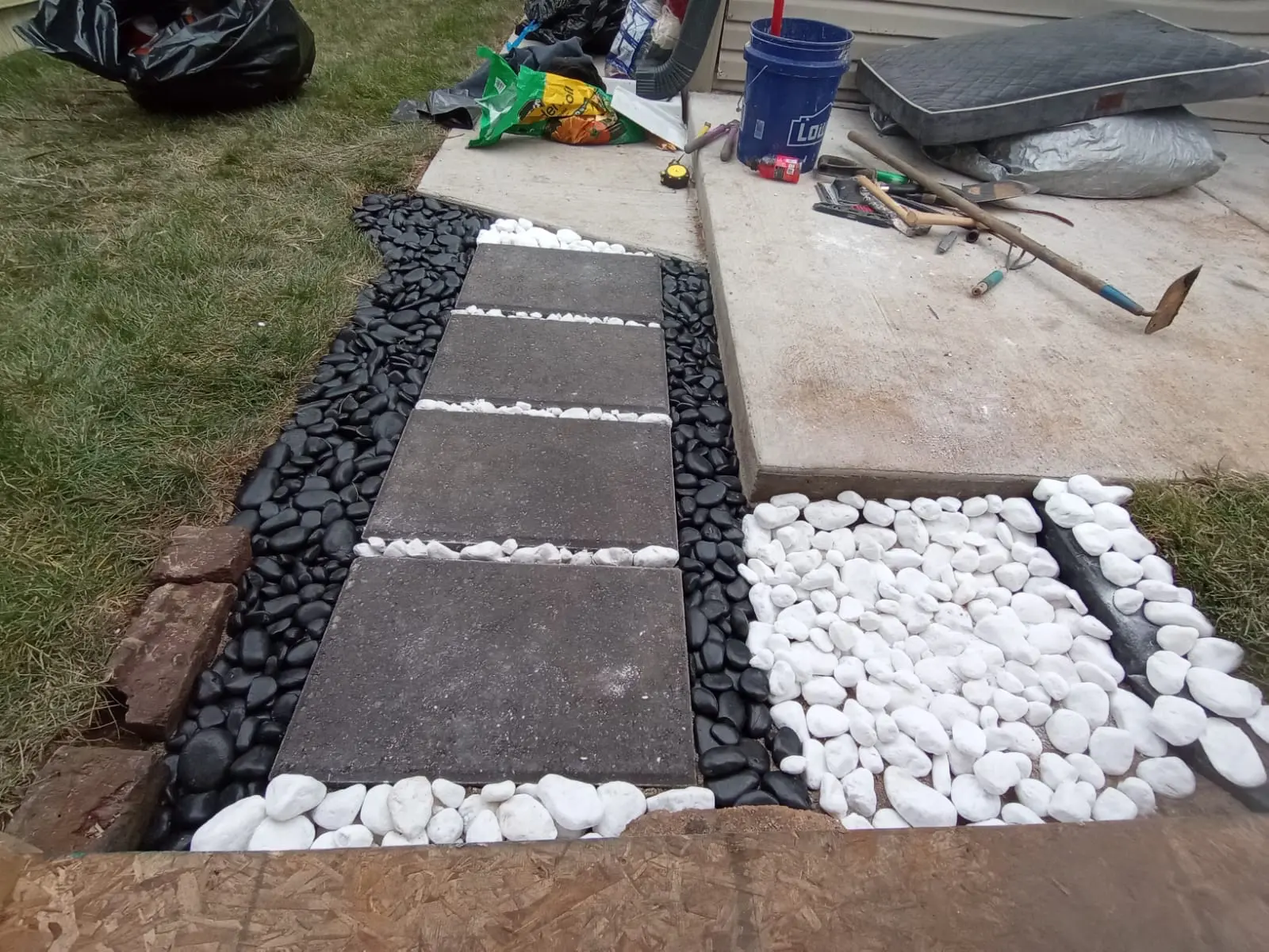 New paver stepping-stone walkway set in black and white river stone beside a concrete patio