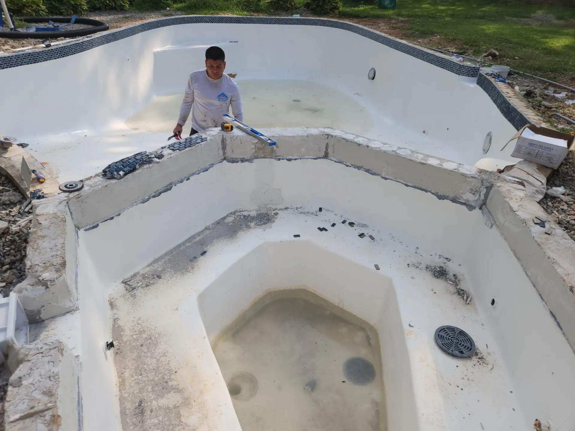 Craftsman setting new mosaic waterline tile on a resurfaced in-ground pool and spa