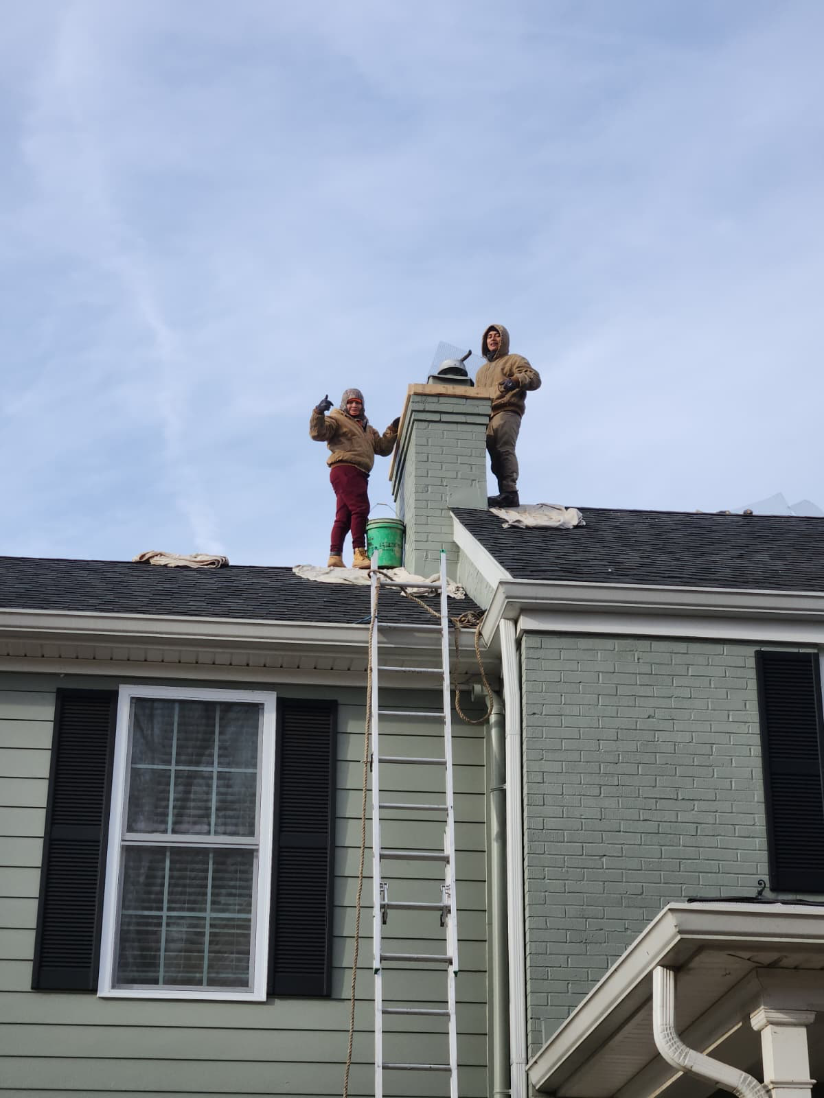 BapuHomes roofers working on a chimney above a shingled roof with drop cloths protecting the shingles