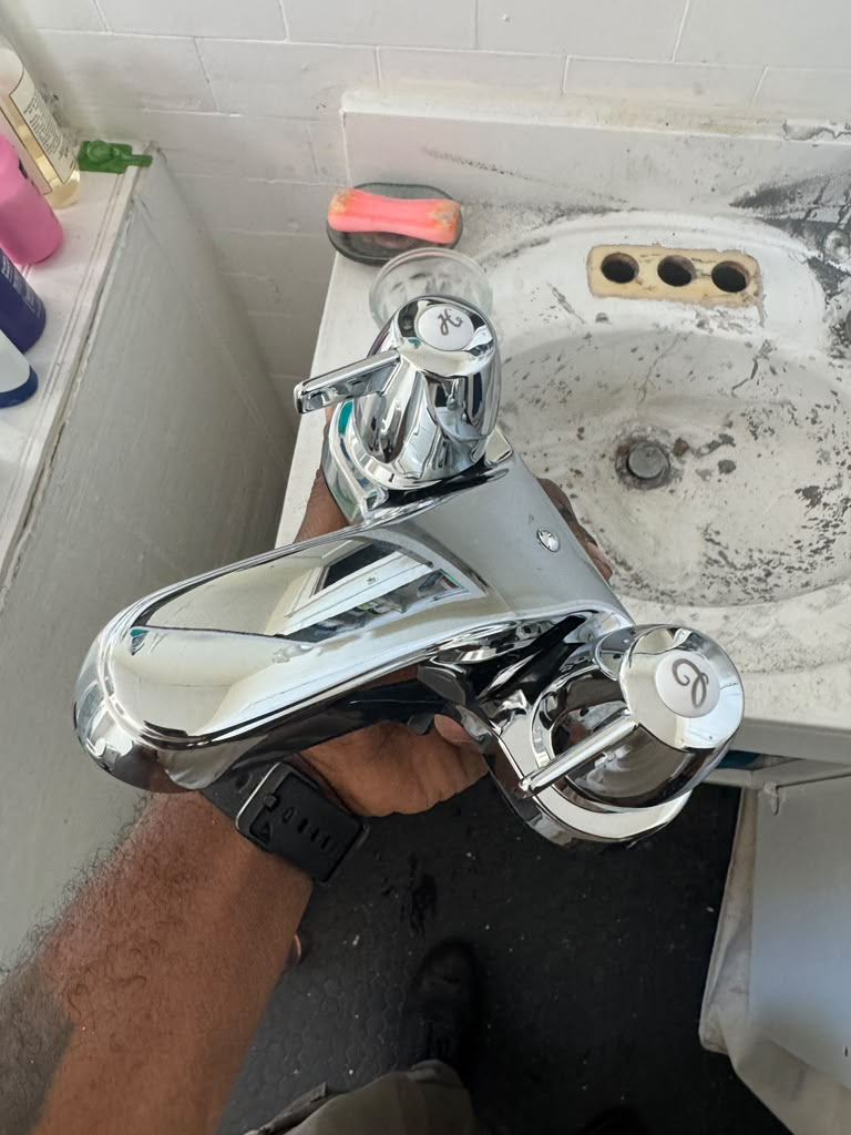 New polished chrome two-handle faucet held above a stained old basin with three empty tap holes