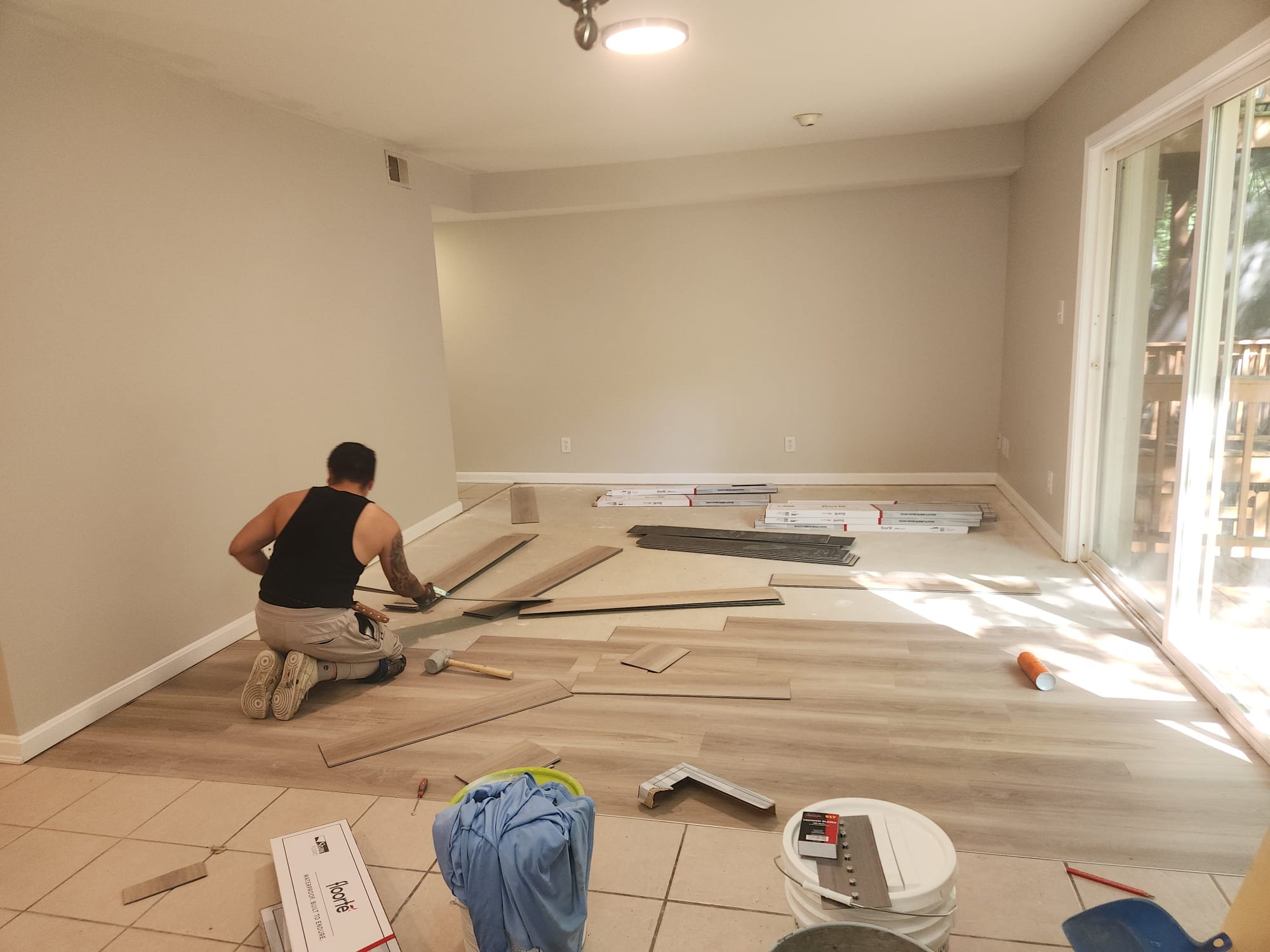 Before: installer laying waterproof LVP planks over the old subfloor in a bare living room