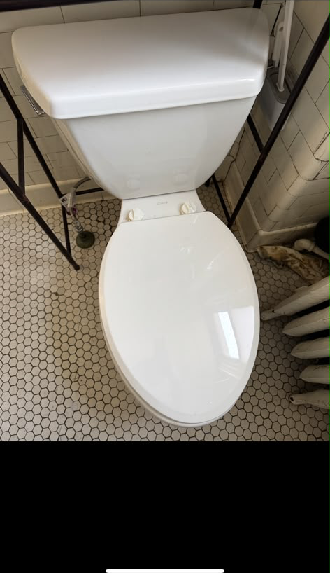 New white toilet installed square to the wall on hexagon tile with the supply line neatly connected