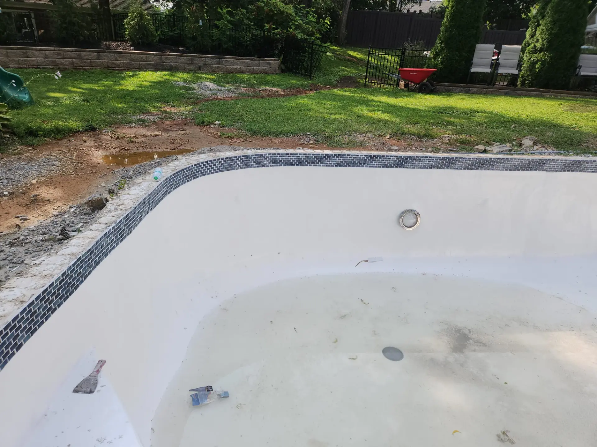 Renovated in-ground pool with fresh white plaster finish and new blue mosaic waterline tile