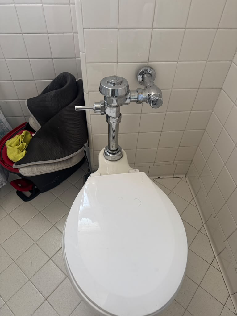 Newly fitted chrome flush valve and angle stop on white tile above a clean toilet bowl